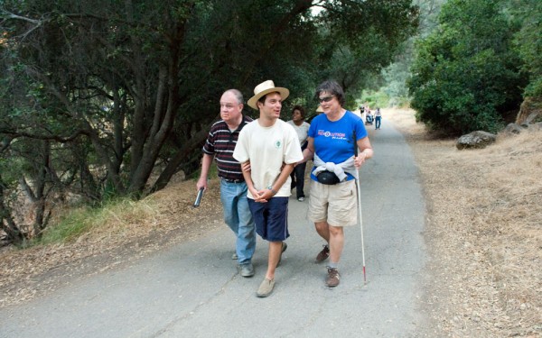 Two hikes with visual impairments are escorted by a sighted guide on a wooded trail