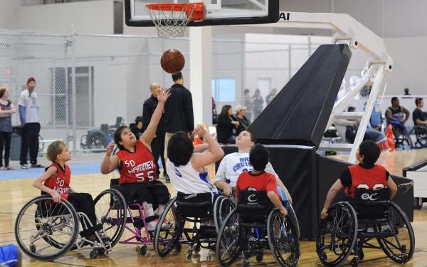 Youth wheelchair basketball players watch a ball pass though the net during a game