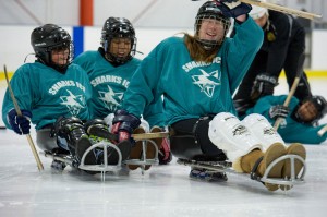 A female sled hockey player waves to the camera with two teammates following