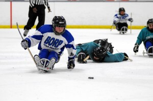 A BORP sled hockey player chases the puck as his opponent does a face plant on the ice