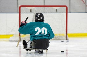A youth sled hockey player faces the goal at the far end of the ice