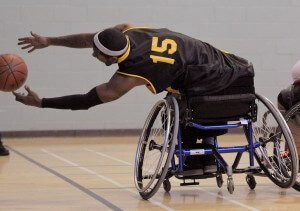 An adult wheelchair basketball player reaches for a ball