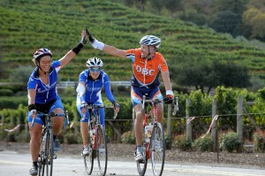 Two cyclists high five while a third looks on