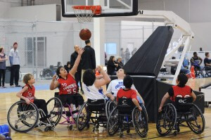 Youth wheelchair basketball players watch a ball pass though the net during a game