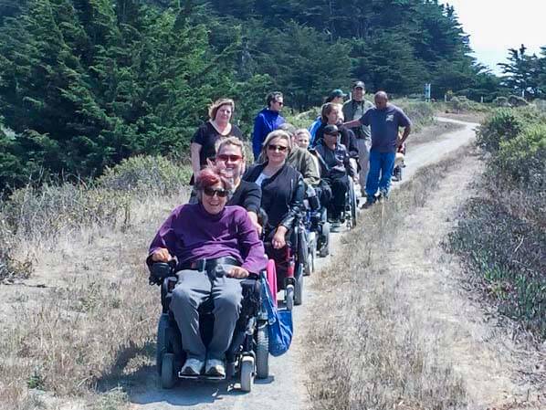 A group of people in wheelchairs and others walking on a trail