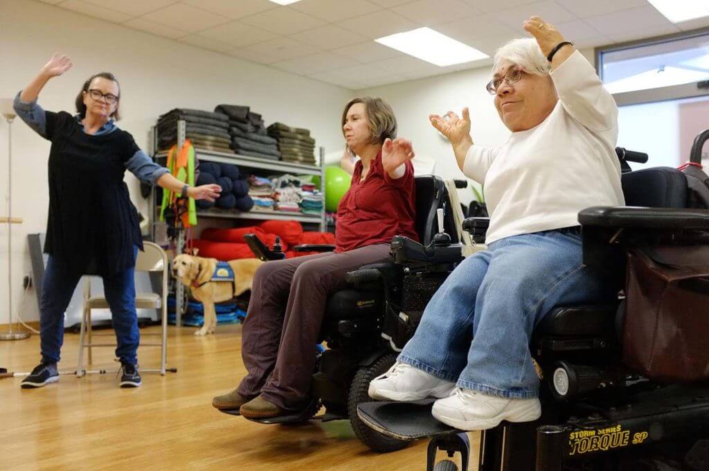 Two women in wheelchairs and one woman standing exercise together