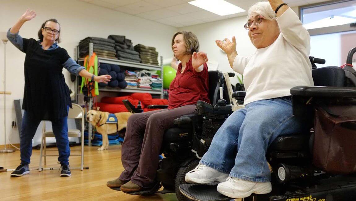 Two women in wheelchairs and one woman standing exercise together