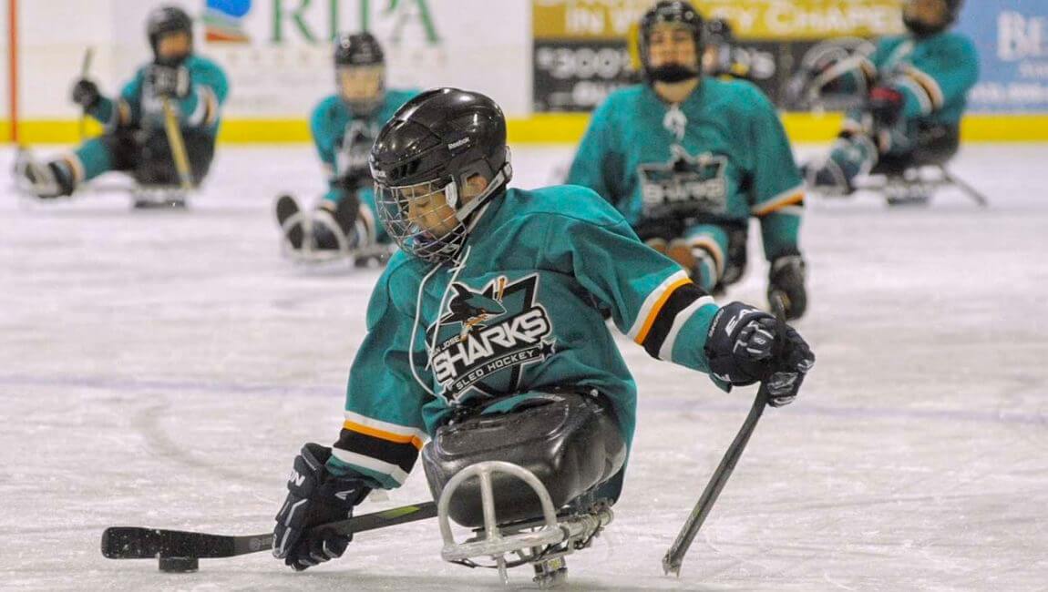 Youth playing sled hockey with team in background