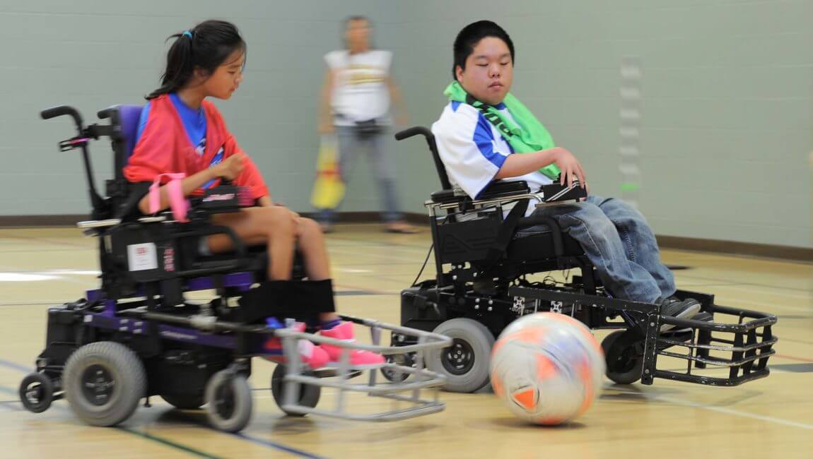 Two young power soccer players chase the ball on court