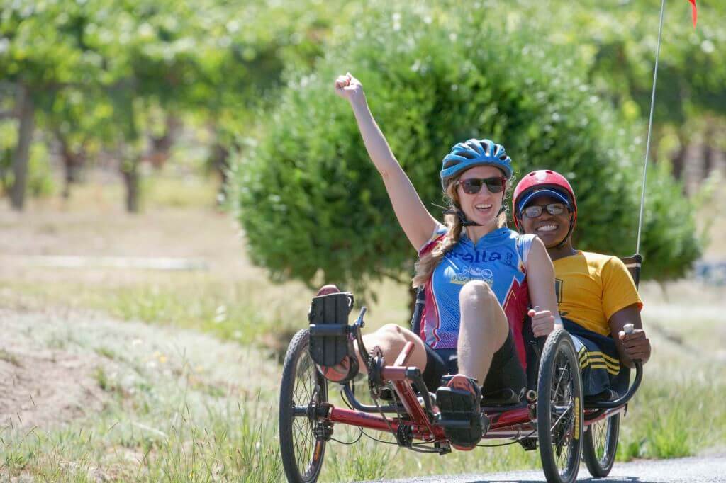 Two riders on recumbent tandem smile and wave