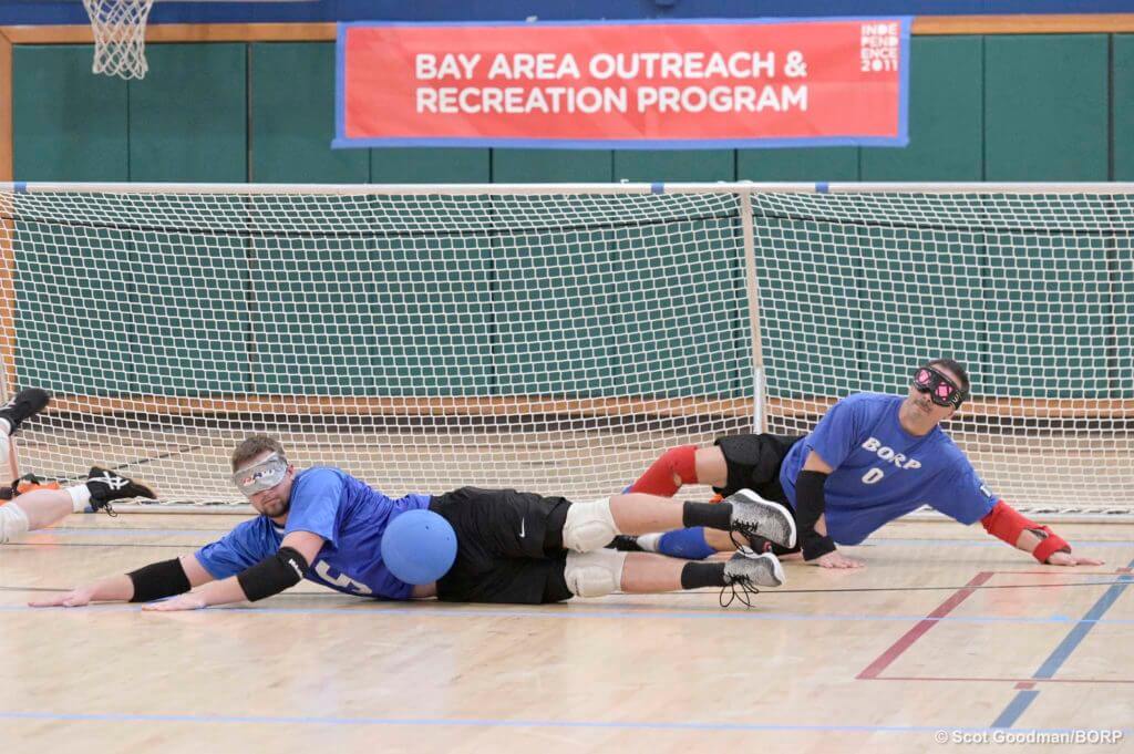 Two male goalball players attempt to block ball