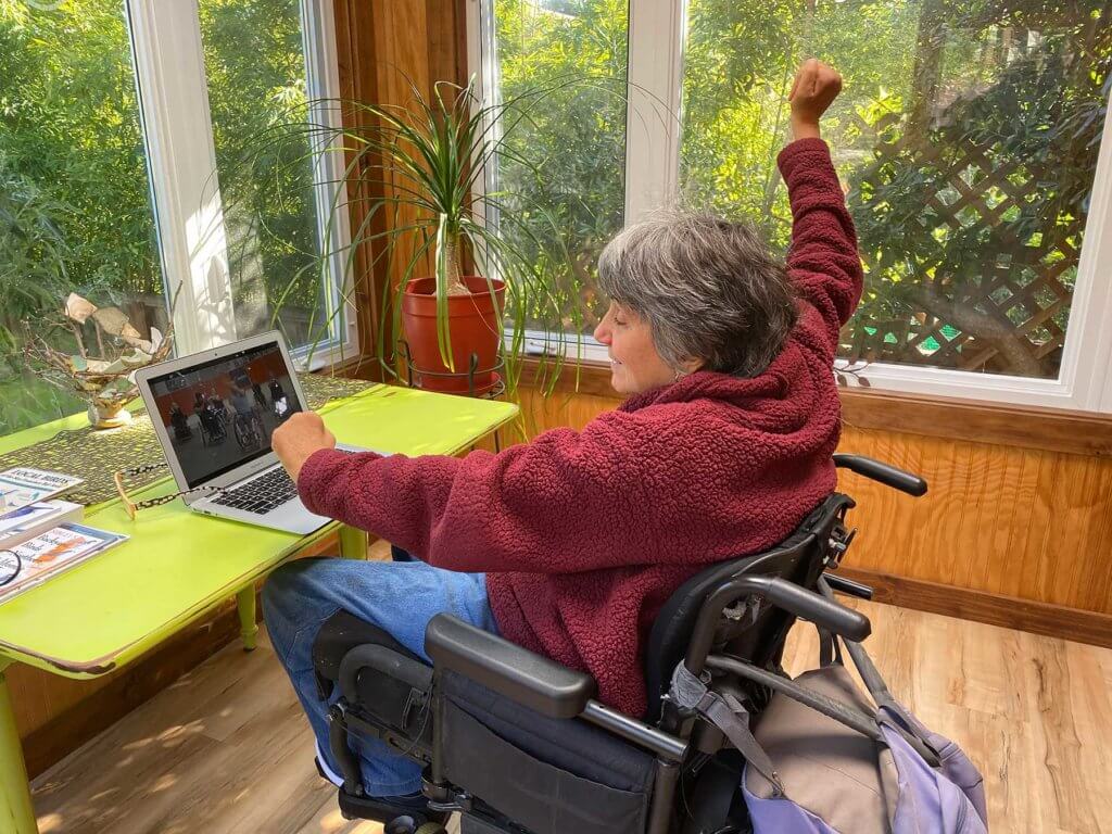 Woman wheelchair user participates in virtual class at home on laptop