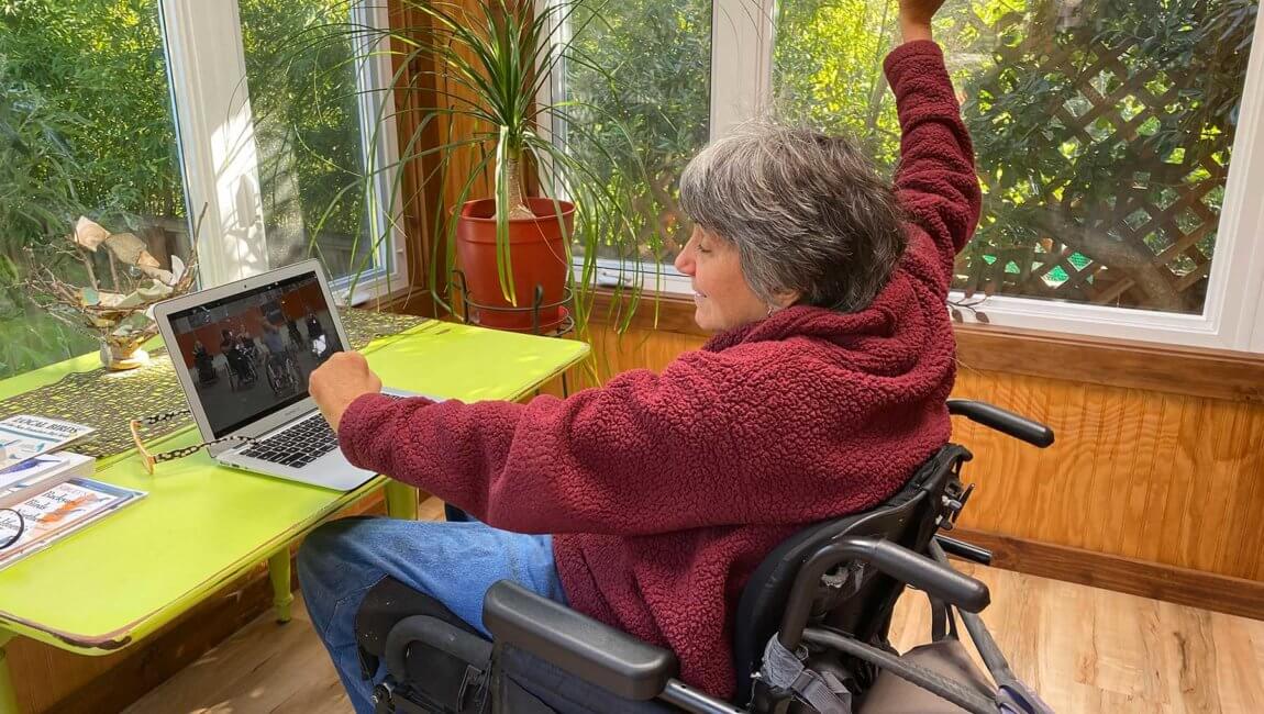 Woman wheelchair user participates in virtual class at home on laptop