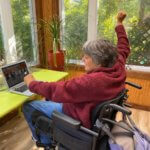 Woman wheelchair user participates in virtual class at home on laptop