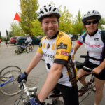 Two people on a tandem cycle, the front person is wearing a 2010 Revolution Ride jersey