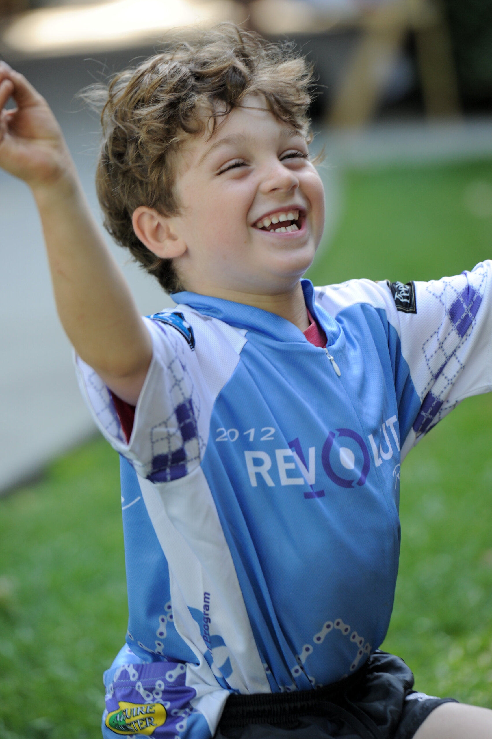 A child wearing the 2012 Revolution Ride jersey with a big smile and arms raised.