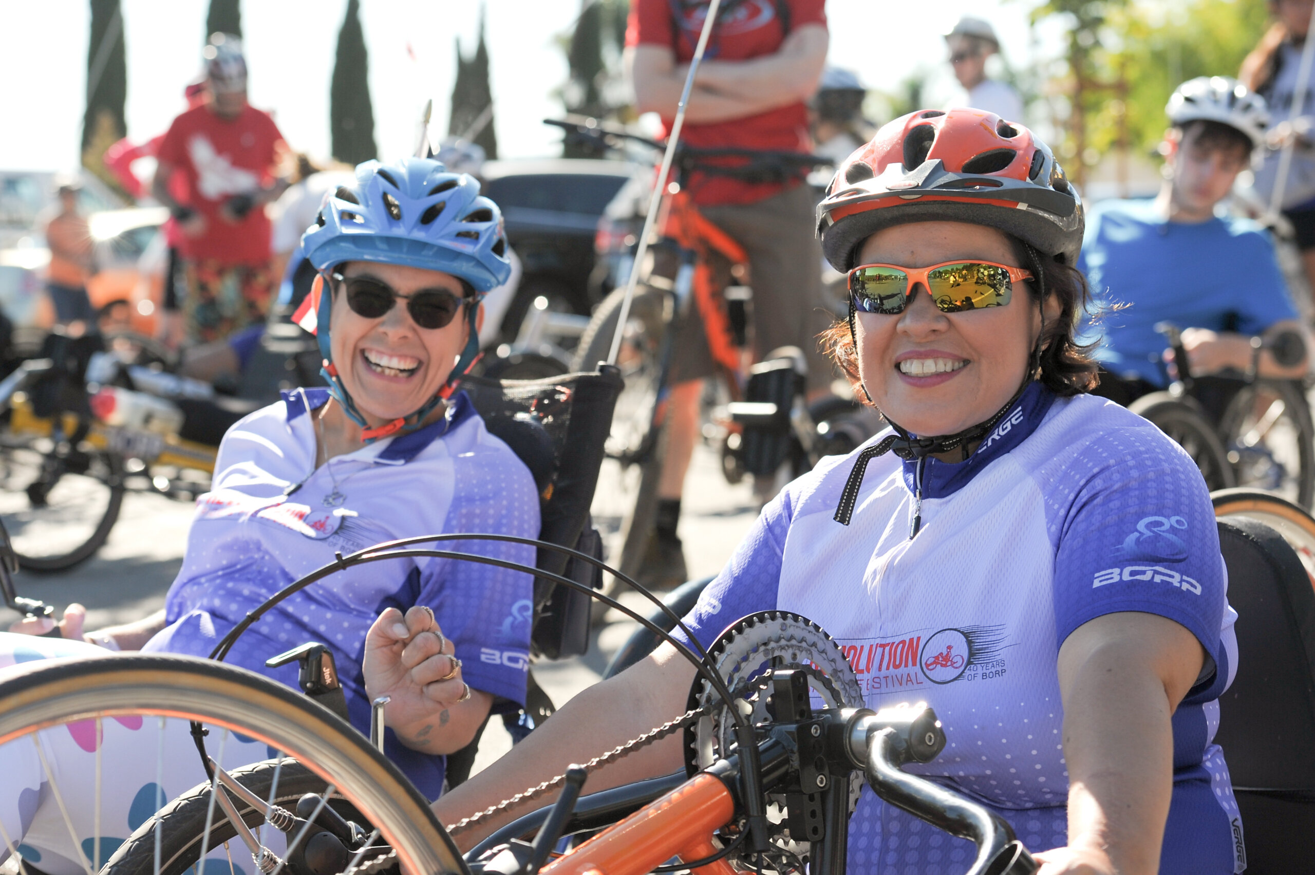 Two women, one in a recumbent cycle and one on a hand-cycle, both wearing the 2016 Revolution Ride.