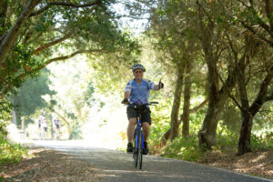 Cyclist riding through the trees giving a thumbs up and wearing a 2019 Revolution Ride jersey.