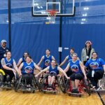 The meteorites, a group of 8 players, pose in sports chairs after their last game with arms linked and smiles.
