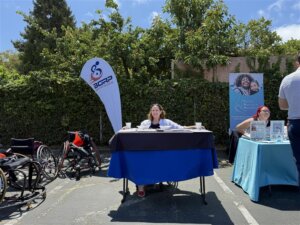 Molly sits at BORP's table smiling at hte camera. The BORP flag and a sports chair is seen in the background. 