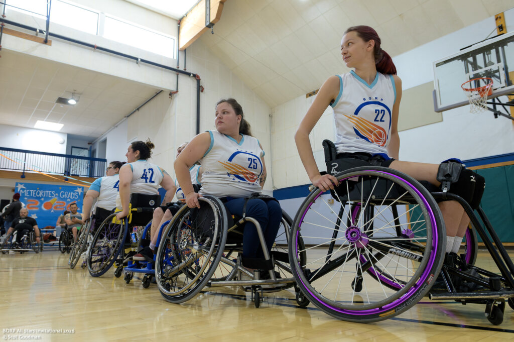 Five wheelchair basketball players line up and look down the court