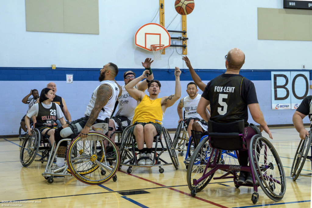 Wheelchair basketball players on opposing teams try to reach a ball in the air