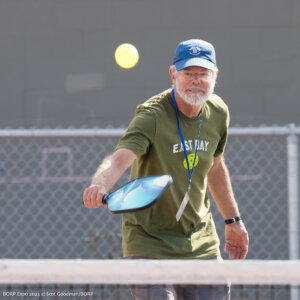 A person hits a yellow pickleball over a net