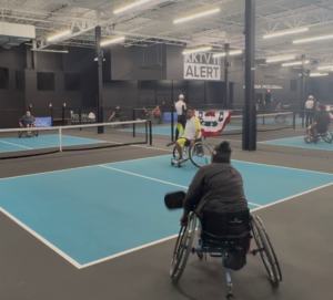 A person in a pickleball wheelchair gets ready to hit a pickleball in motion