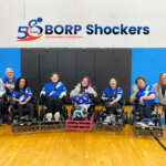 BORP Shockers power soccer team posing in gym 5 athletes using power chairs, and 3 coaches