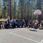 Power wheelchair users and camp ambulatory people posing on an outdoor basketball court with forest in the background